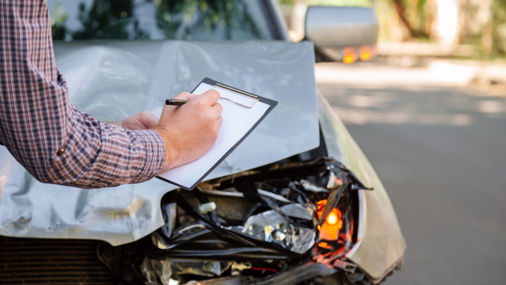man writing car insurance claim at the scene of a car accident